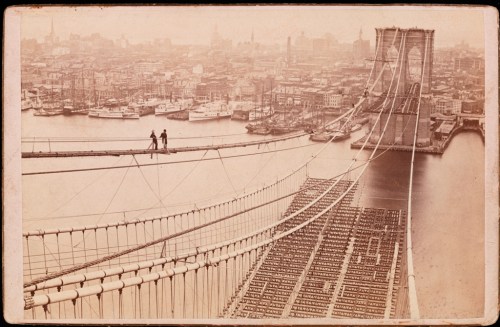 Men walking on cables during the construction of the Brooklyn Bridge.