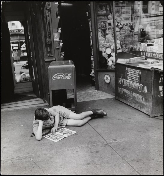 John Albok (1894-1982). Boy reading comics in front of newspaper store, west side of Madison Avenue between 96th and 97th Streets. 1933-1934. Museum of the City of New York. 82.68.11. 