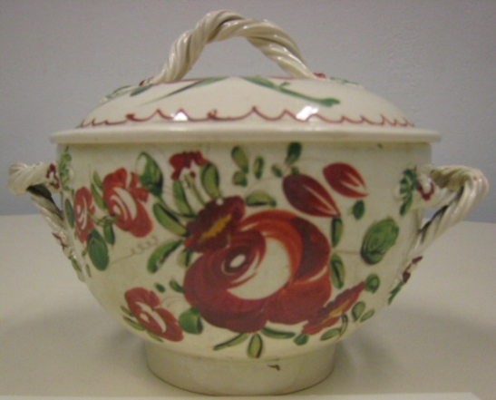 Cream-colored earthenware sugar bowl from tea service with enamel decoration of large red roses and polychrome leaves and flowers, twisted handle on each side and circular cover with same twisted handle at the top center.