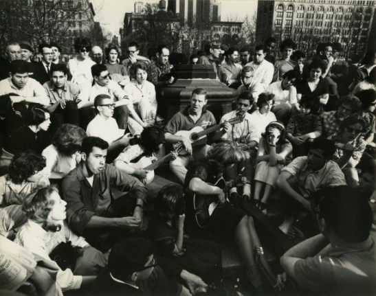View of young people gathered around three people playing guitar at Washington Square Park.