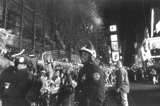 A smiling police officer is watching the screaming crowd celebrating New Year's Eve 1997 behind police lines on Times Square.
